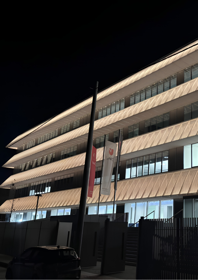 UNIC Athens Campus building at night, showcasing the illuminated facade and UNIC flags. View of UNIC.png