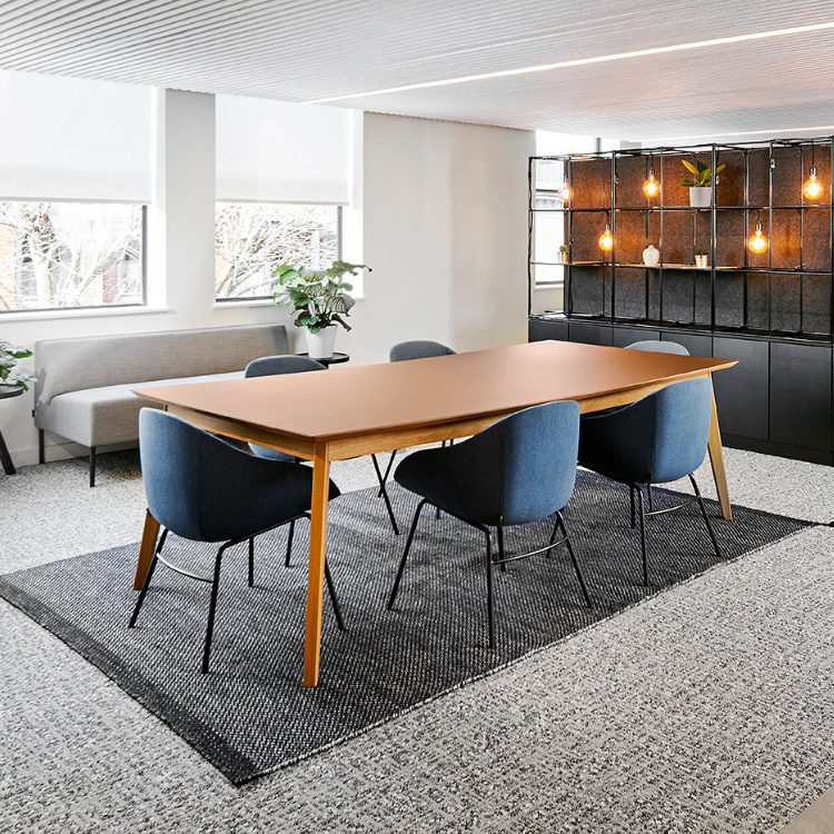 Dalby Table with a warm wood finish and slender profile, surrounded by blue upholstered chairs in a modern office space.