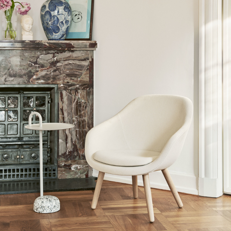 AAL 82 lounge chair in cream upholstery with solid oak legs set in a cozy living room next to a marble fireplace.