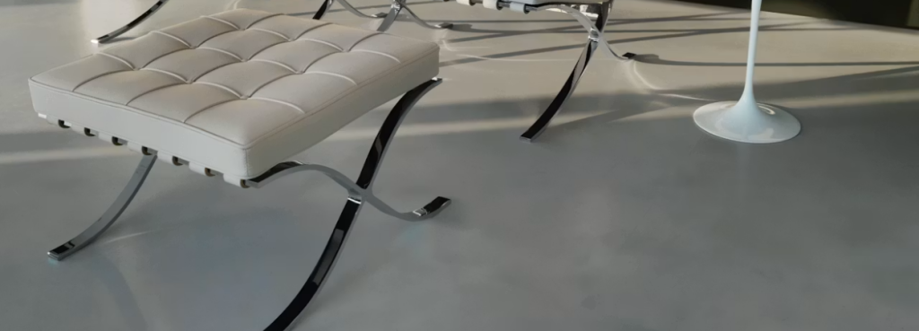 Minimalist cream Barcelona Stool with polished stainless steel base sitting on a sleek floor in natural light.