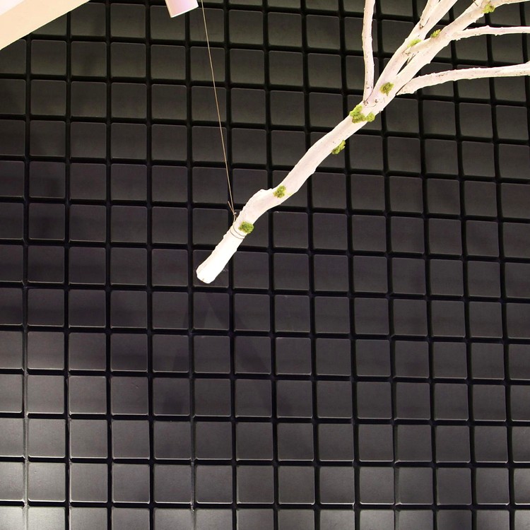 Deeply textured Key Grid acoustic wall featuring dark, raised squares and a decorative white twig branch.