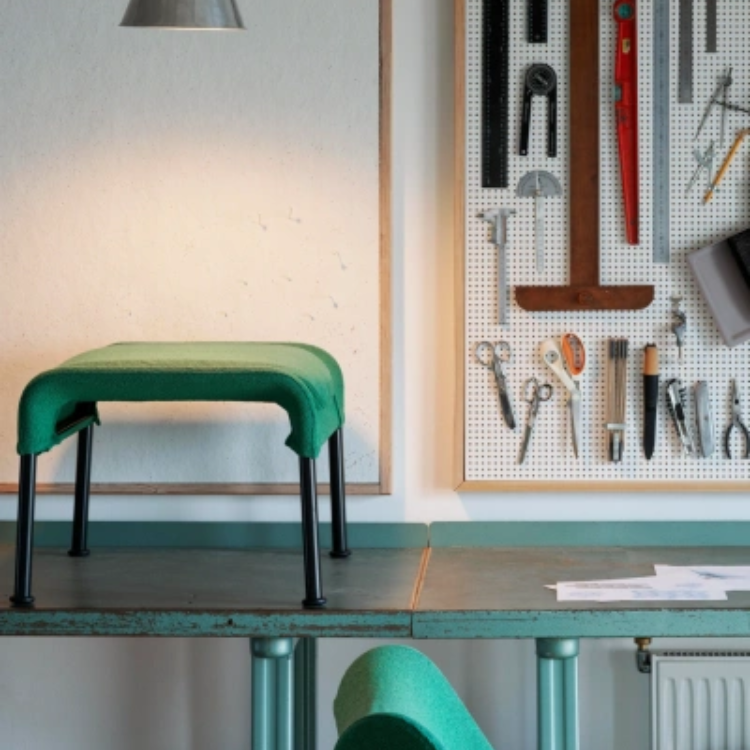 Green O2 Ottoman with black legs placed on a workspace table next to a pegboard of tools.