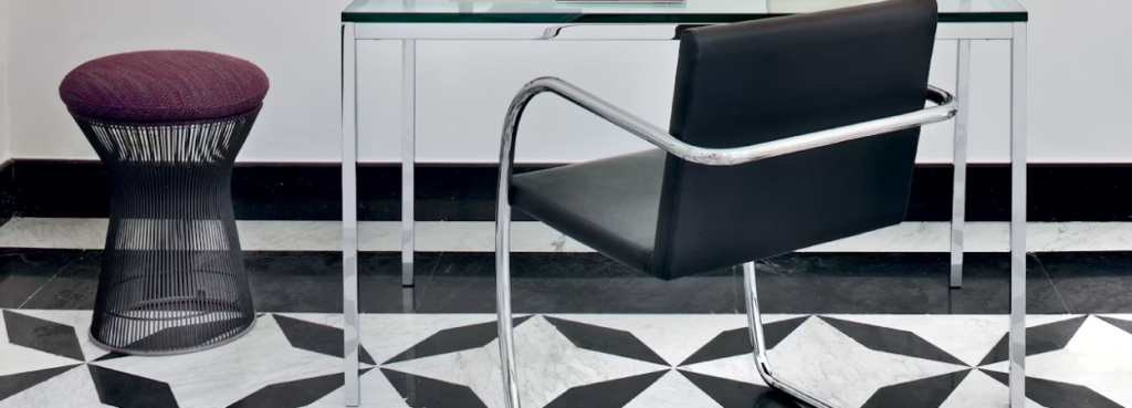 Platner Stool with dark steel wire base and textured berry-colored cushion placed beside a sleek glass-topped desk.