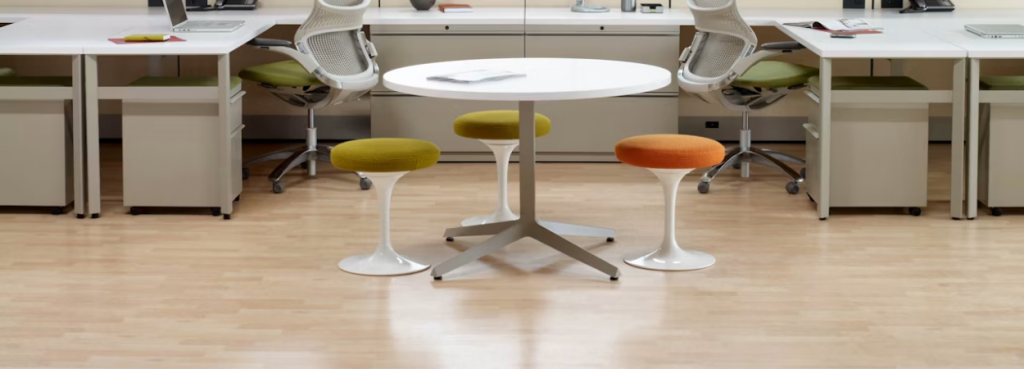 Three colorful Knoll Tulip Stools with fabric cushions arranged around a central white table in a bright workspace.