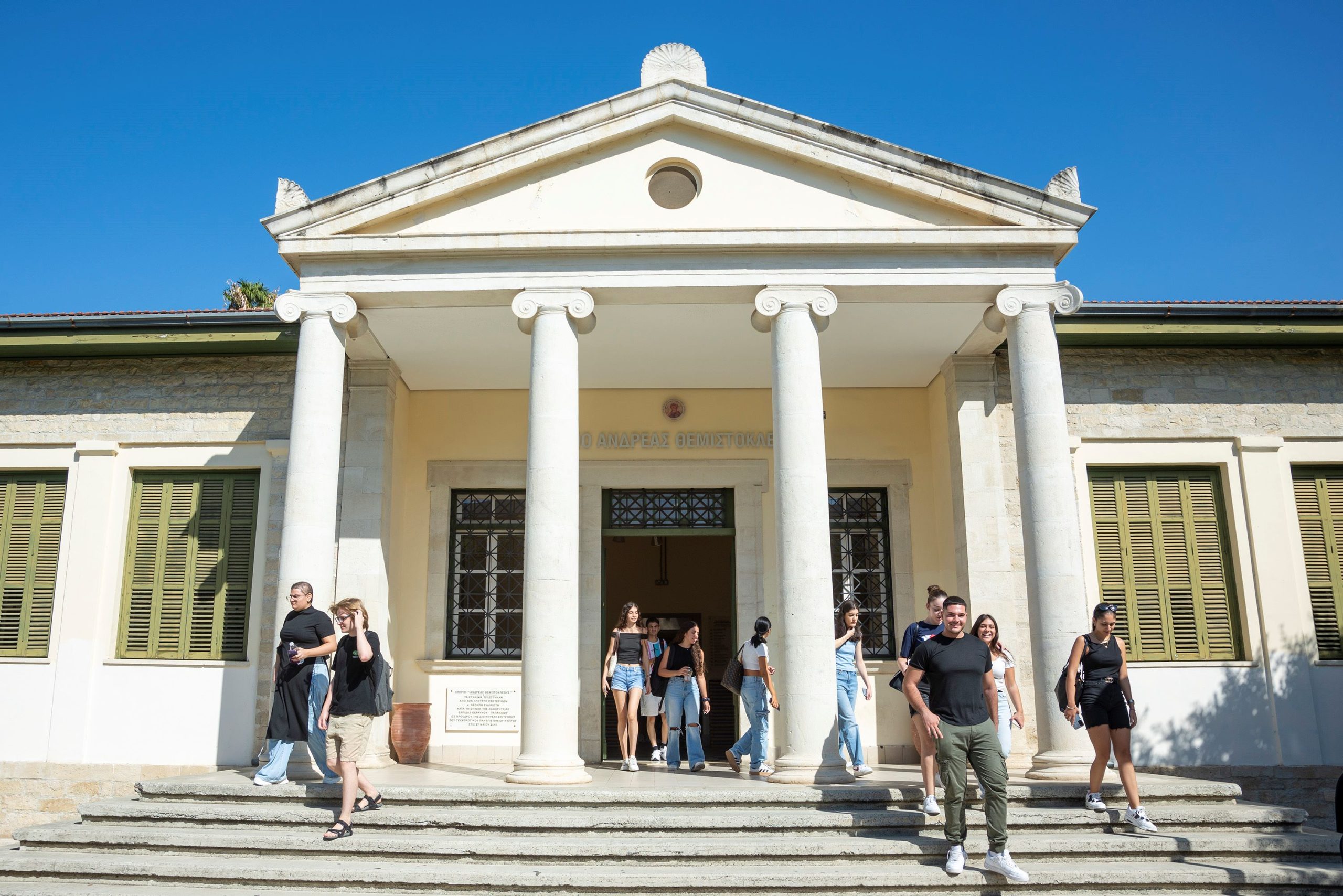 Students exit a neoclassical building at the Cyprus University of Technology under a pediment supported by white columns.