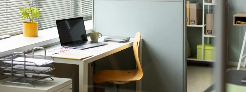 Modern office workstation setup with a laptop, wooden chair, and desk accessories for a hybrid workplace environment.